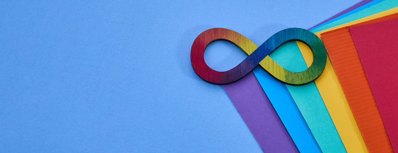 Rainbow infinity symbol sits against a sky blue background with coloured sheets of paper