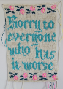 Needlework by Emily Robbins. White panel with blue text that reads "Sorry to everyone who has it worse" with a top and bottom border of pink flowers